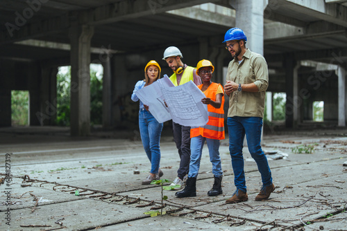 Group Construction workers looking at blueprints on construction site. Construction industry concept - architects and engineers discussing work progress between concrete walls, scaffolds and cranes.