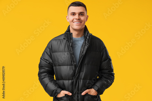 Young man in black stylish puffer jacket on yellow background photo