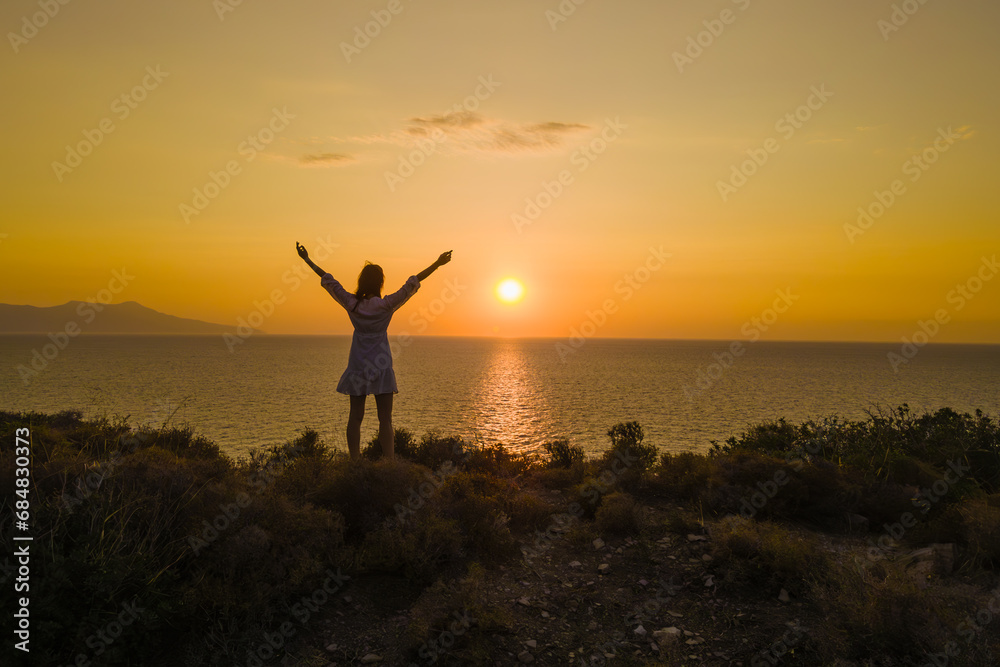 Young woman rising hands on mountain top above sea aerial. Female tourist standing on cliff at seaside. Lady admires tropic seascape, Active tourism lifestyle