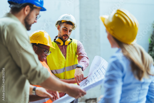 Group of multiethnic industrial employees planning building project and meeting on panoramic terrace. Four international colleagues using computer and technical plan for remodeling business center.