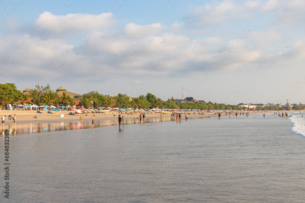 BALI, INDONESIA - OCTOBER 10, 2023: Tourists and locals on famous Kuta beach in Kuta, Bali. This is the perfect place for learning surfing.