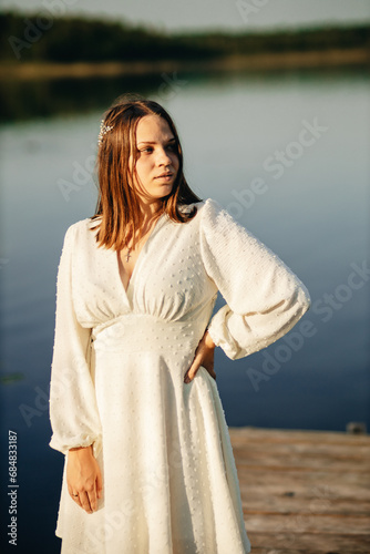 a girl in a white dress sits on a bridge on a lake in sunset in summer © Марина Шемедюк