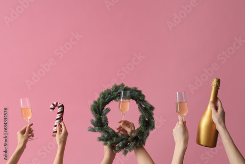 Female hands with glasses of champagne and wreath on pink background