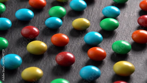 Sweet dragees in colored glaze rotating on black plate background macro side view sun light. Delicious sweets and candies close-up that children like. Chocolate Coating photo