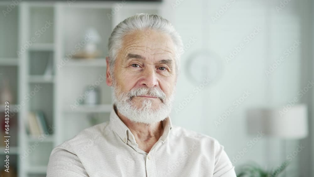 Close up portrait of a happy older man with gray hair standing in bright living room at home. Handsome senior retired male looking at camera. Headshot of confident smiling mature bearded grandfather Close up portrait of a happy older man with gray hair standing in bright living room at home. Handsome senior retired male looking at camera. Headshot of confident smiling mature bearded grandfather