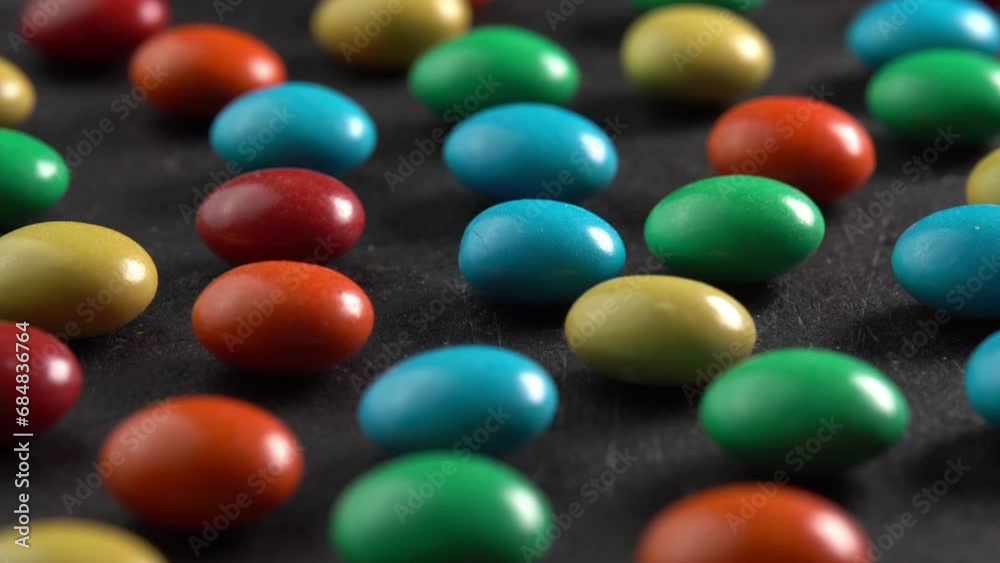 Sweet dragees in colored glaze rotating on black plate background macro side view low light. Delicious sweets and candies close-up that children like. Chocolate Coating Sweet dragees in colored glaze rotating on black plate background macro side view low light. Delicious sweets and candies close-up that children like. Chocolate Coating