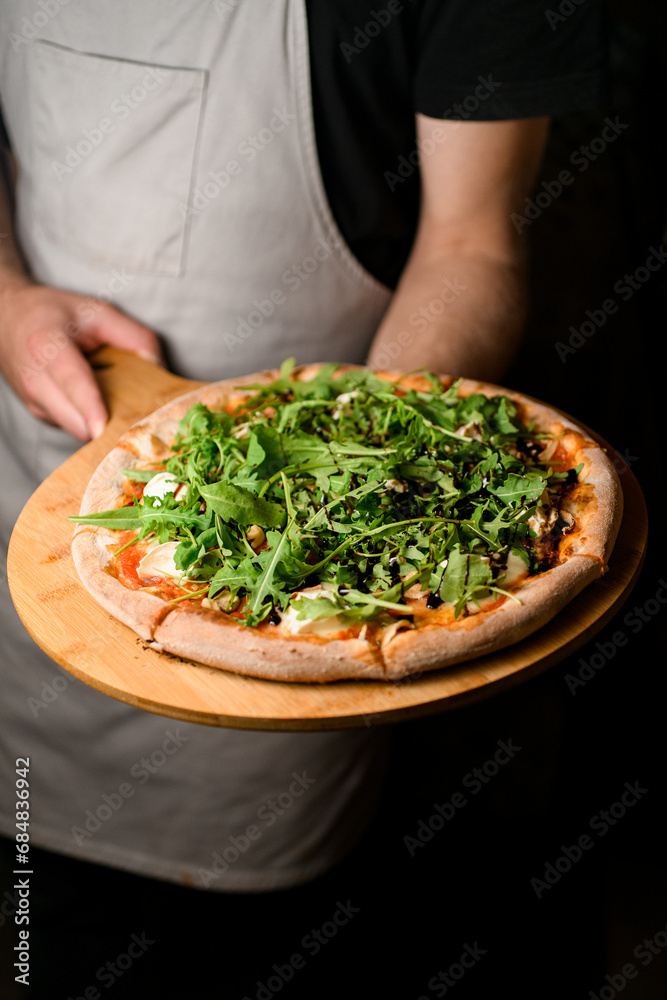 Fresh and aromatic pizza with vibrant arugula, which the chef presents on a wooden tray.