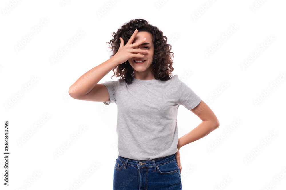young european woman with black curly hair in a gray basic t-shirt looks happy on a white background young european woman with black curly hair in a gray basic t-shirt looks happy on a white background