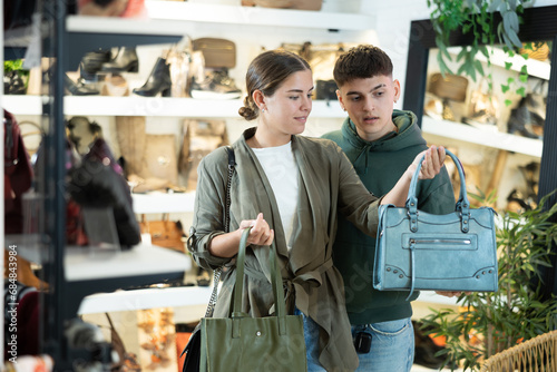 Young man with girl friend inspects shop window and is looking for modern, fashionable and roomy shoulder bag. In leather goods store, customers make choice of product with reasonable price