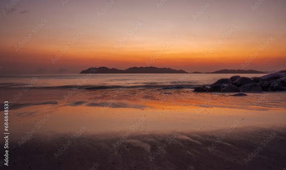 Before sunrise an orange glow with reflections on water, rocks and the wet patterned sand of a tropical beach at Rose Bay in Bowen, part of the Whitsunday region in tropical Queensland, Australia.