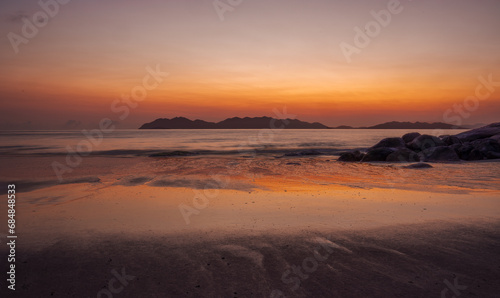 Before sunrise an orange glow with reflections on water, rocks and the wet patterned sand of a tropical beach at Rose Bay in Bowen, part of the Whitsunday region in tropical Queensland, Australia. © Shirley and Johan