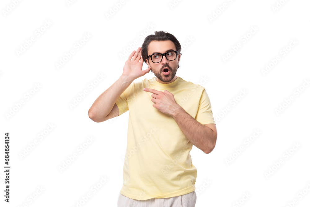 Fototapeta premium young handsome european brunette guy with a beard and mustache in glasses stands in surprise on a white background with copy space