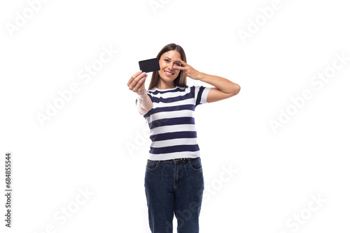 young brunette caucasian woman with light makeup dressed in a striped t-shirt and jeans holds out a plastic credit card with a mockup