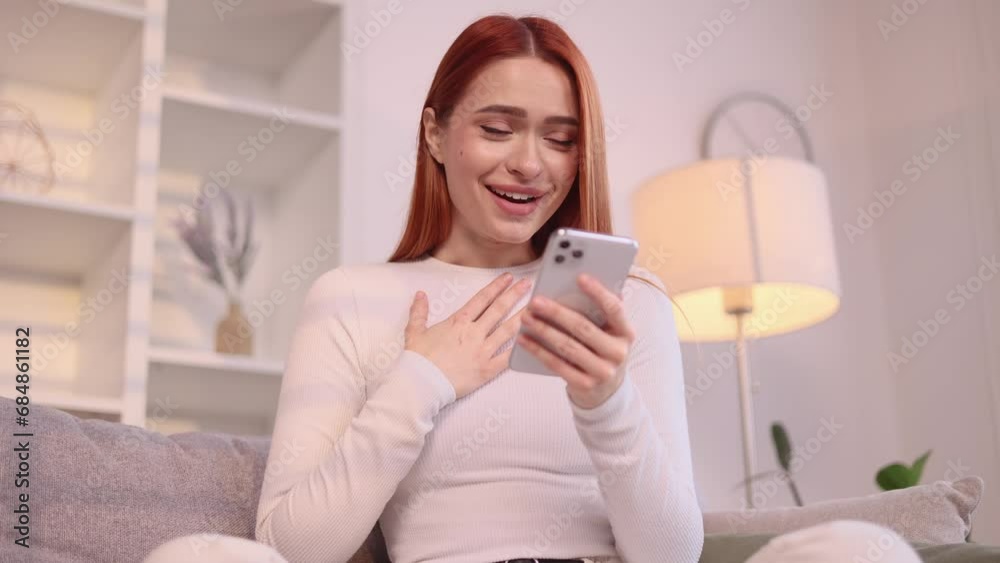 Amazed lucky red haired woman extremely happy after read message on mobile phone at home Excited cute female pleased rejoices received great news on smartphone indoors Amazed lucky red haired woman extremely happy after read message on mobile phone at home Excited cute female pleased rejoices received great news on smartphone indoors