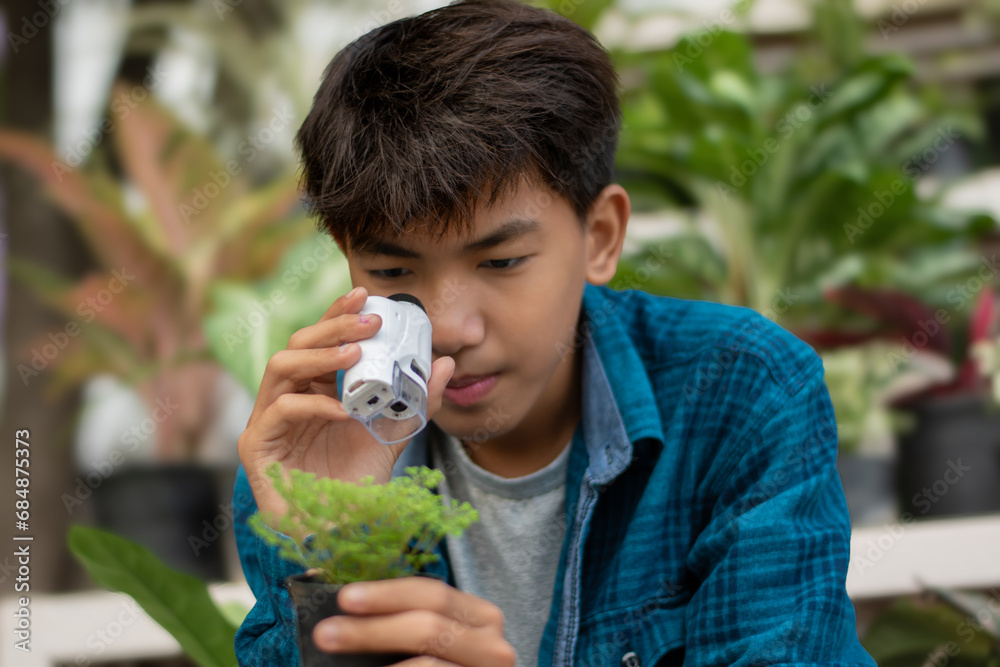 Asian cute schoolboy holds mini portable microscope and looking at the small details of the potted plant in his hand to study and relax through the lens, soft focus. Asian cute schoolboy holds mini portable microscope and looking at the small details of the potted plant in his hand to study and relax through the lens, soft focus.