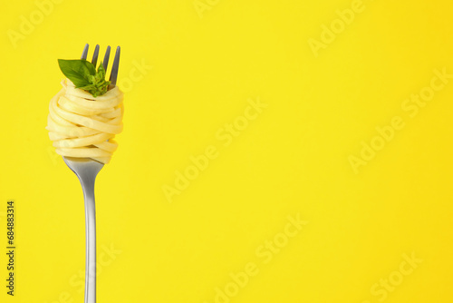 Fork with tasty pasta and basil on yellow background, space for text