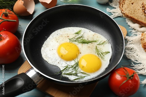Frying pan with tasty cooked eggs, dill and other products on light blue wooden table