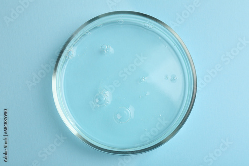 Petri dish with liquid sample on light blue background, top view