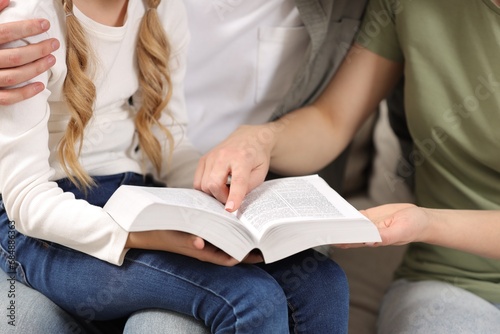 Girl and her godparents reading Bible together indoors, closeup
