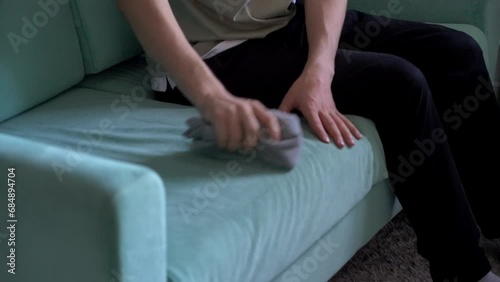 worker with yellow microfiber rag cleaning sofa textile at home