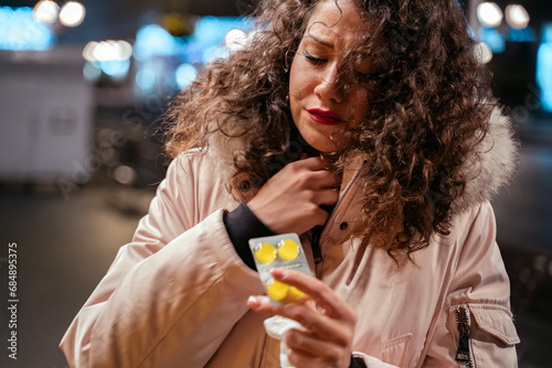 Young woman in the city streets in winter having sore throat and using lozenges  photo