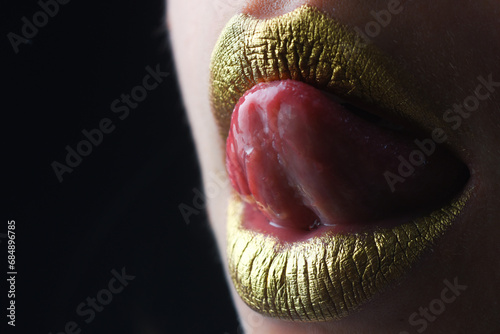 Sexy tongue licking lips. Gold paint on mouth. Golden lips. Luxury gold lips make-up. Golden lips with creative metallic lipstick. Gold metal lip. Sensual woman mouth, clse up, macro. photo