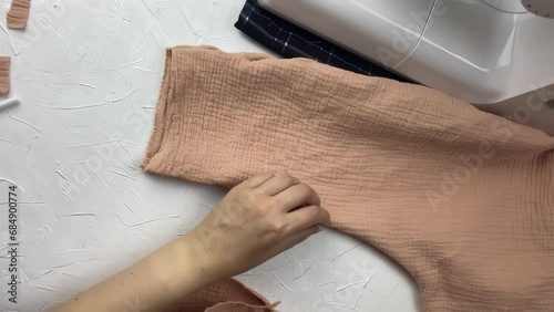 Seamstress cut off extra thread on a cotton muslin fabric with scissors. Workshop of a fashion designer. Needlewoman checks the seams and the appearance of the new clothes. Craft and hobby.