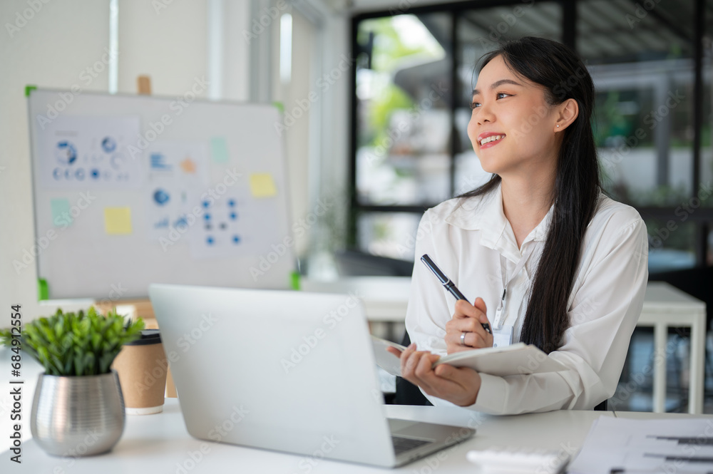 Young beautiful Asian businesswoman working for her client in her office room with laptop and office supplies. Young beautiful Asian businesswoman working for her client in her office room with laptop and office supplies.