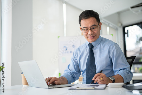 Experienced senior businessman working on his project in his office room. Using laptop computer.