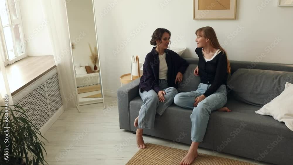 Two girlfriends or sisters talking and laughing at home on the couch Two girlfriends or sisters talking and laughing at home on the couch