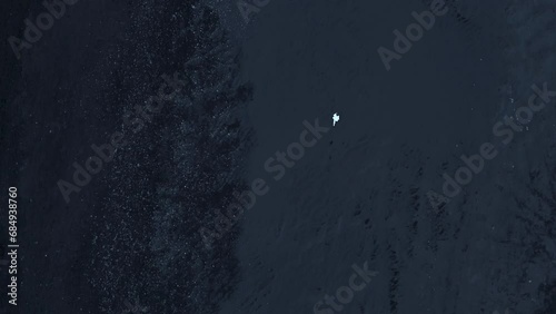 Long and vast coastline in Iceland with volcanic black-sanded beach and a running man looking like a small white spot on a famous mysterious shore. High quality 4k footage