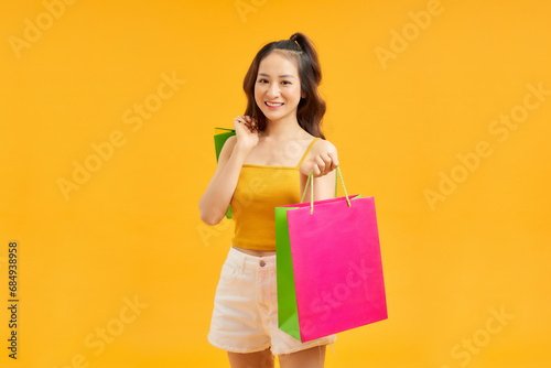 Pretty Asian woman carrying colorful shopping bags in vivid yellow background