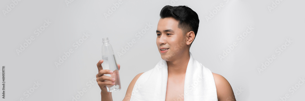 young smiling muscular athlete man with a white towel on his shoulder holding a water bottl young smiling muscular athlete man with a white towel on his shoulder holding a water bottl