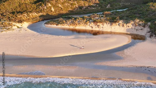 Surfers walk over ocean inlet in Margaret River at sunset photo