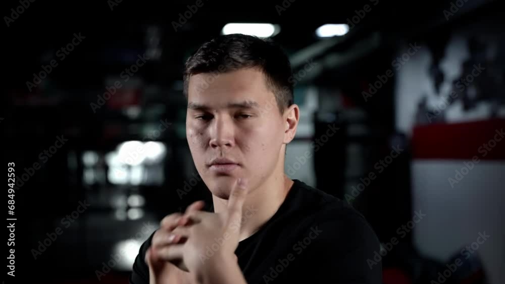 Man kneading his fists before training, close-up of a boxer in a black t-shirt. Preparation for battle. Exercise in the gym. Man kneading his fists before training, close-up of a boxer in a black t-shirt. Preparation for battle. Exercise in the gym.