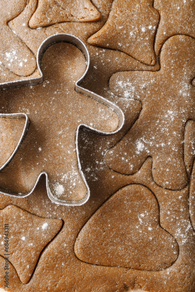 Cooking ginger cookies, Christmas and New Year traditional cookies in shape of gingerbread man, raw rolled out dough with cut out dough figures, closeup texture, top view, metal pastry cutter on dough