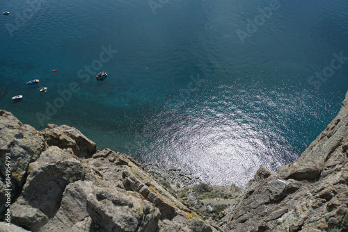 Looking down at a glittering lake with boats from the top of a cliff