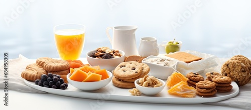 Above the white background, a healthy spread of food is placed on the table, showcasing a variety of tea, bakery goodies, plates full of healthy snacks, biscuits, and cookies. A cup of delicious drink