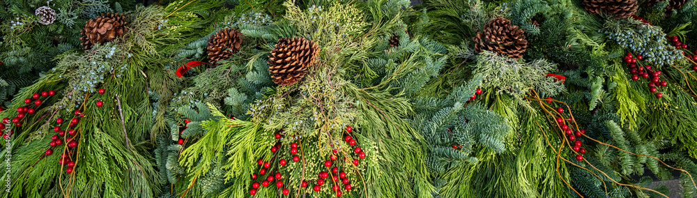 Fototapeta premium Fresh Christmas decorative greenery for sale, door hangings and potted table décor, made out of fresh evergreen branches, pinecones, and red berries 