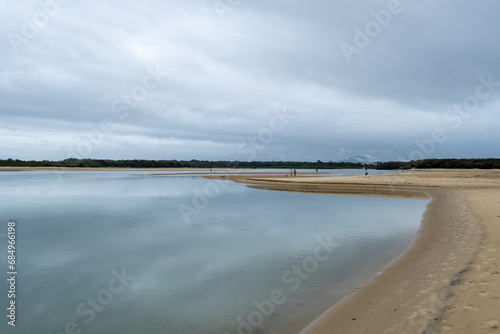 Cotton Tree at the mouth of the Maroochy River  Queensland  Australia. People fishing and walking around the beach on low tide. Reflection of cloudy sky in the water.
