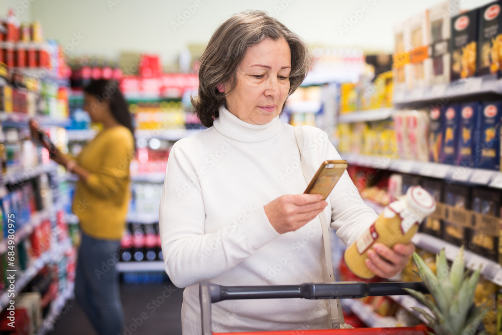 Elderly shopper using smartphone scans qr code on label in grocery supermarket