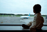 Interested toddler girl sits on windowsill of panoramic window in airport terminal. Silhouette of child looks at planes waiting for flight