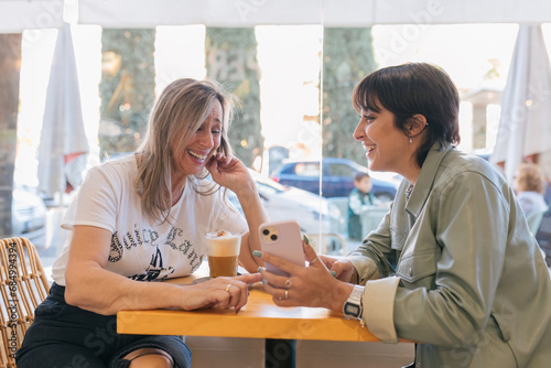 Cheerful girlfriends with smartphone and coffee in cafe