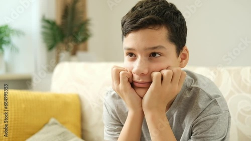 Caucasian boy sitting on sofa watching tv in living room. Side view of focused brunette teen boy sitting in front of tv screen watching film in evening at home.