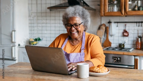 old grandmother happy smile uses her laptop in the kitchen to make video calls with friends 