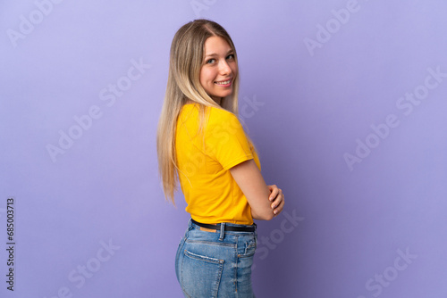 Young blonde woman isolated on purple background looking to the side and smiling