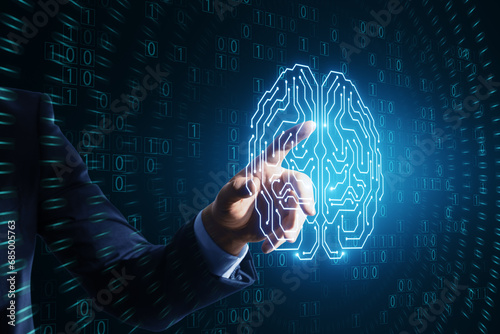 Close up of businessman hand pointing at glowing brain hologram with binary coding on blue background. Programming, machine learning and artificial intelligence concept.