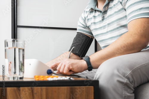 Unrecognizable man sitting on a sofa at home and measures blood pressure on a hand with modern digital tonometer