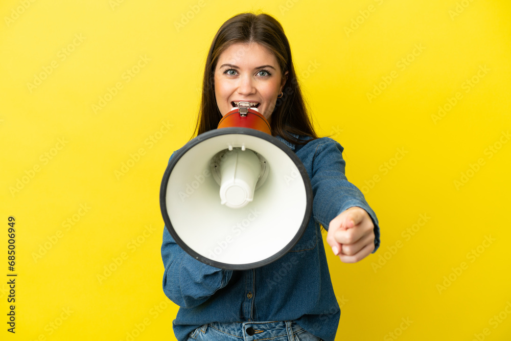 Young caucasian woman isolated on yellow background shouting through a megaphone to announce something while pointing to the front Young caucasian woman isolated on yellow background shouting through a megaphone to announce something while pointing to the front