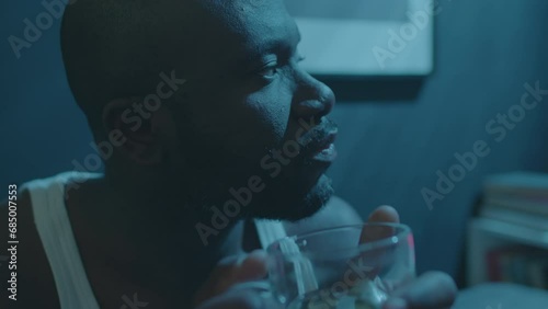 Close up shot of sleepless African American man drinking herbal tea in dark bedroom while trying to cope with insomnia at night